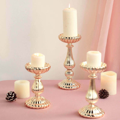 Elegant decorative candle holders with lit candles on a soft pink surface.