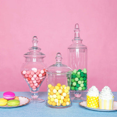 Colorful candy jars with pink, green, and yellow sweets on a pastel backdrop.