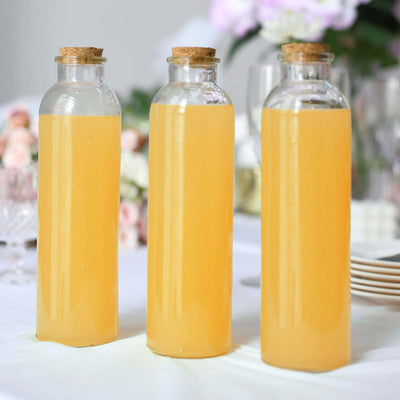 Three glass bottles filled with yellow beverage on a table.