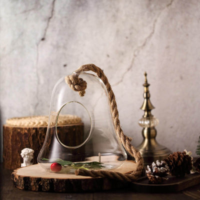 Glass terrarium with rope handle and decorative greenery on wooden base.