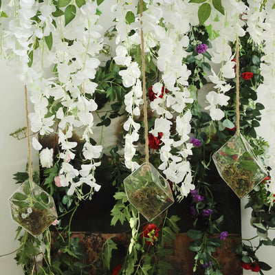 Hanging terrarium with white flowers and greenery in a vibrant floral backdrop.
