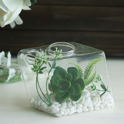 Succulent terrarium in a glass container with decorative stones and greenery.