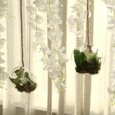 Hanging glass planters with greenery against a soft, flowing curtain backdrop.