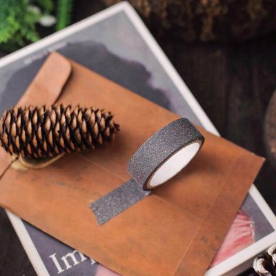 Decorative black washi tape on a brown envelope with a pine cone.