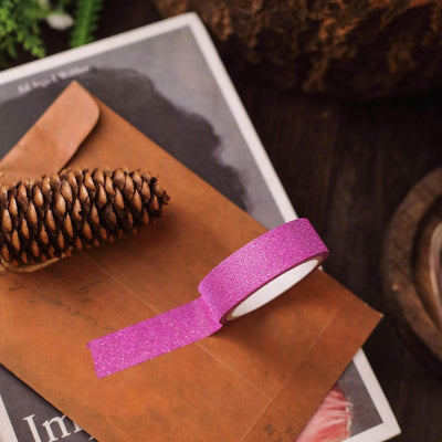 Pink glitter tape on a brown envelope with a pinecone and nature backdrop.