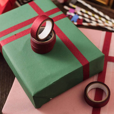 Green gift box with red ribbon and tape rolls on a wooden surface.
