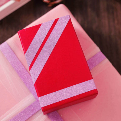 Red gift box with pink glitter stripes on a pink background.