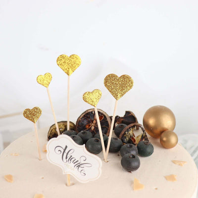 Gold glitter heart cake toppers on a decorated dessert with blueberries.