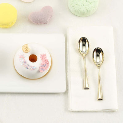Decorative donut with pink icing and two gold spoons on a napkin.