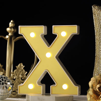 Yellow marquee letter "X" with lights on a dark background.