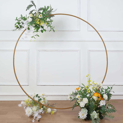 Floral arrangement with hoop and greenery on a wooden floor backdrop.