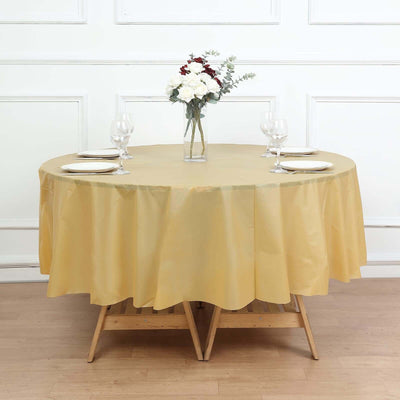 Round gold tablecloth draped over a table with a vase and glasses on a wooden floor.