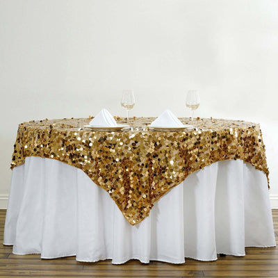 Gold sequin tablecloth draped over a round table with wine glasses and napkins.