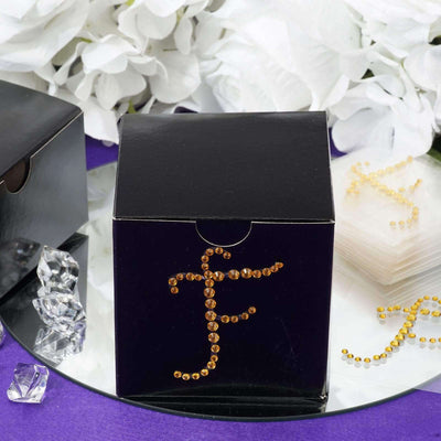 Black box with rhinestone "F" design on a mirrored surface.