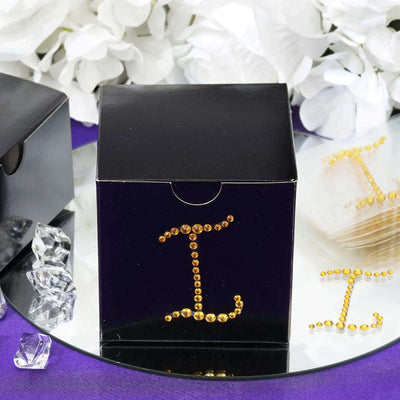 Black gift box adorned with golden rhinestones on a reflective surface.