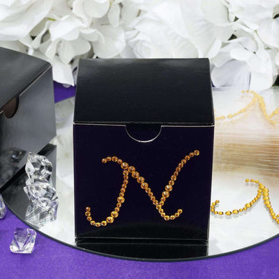 Black gift box with shiny gold "N" decoration on a mirrored surface.