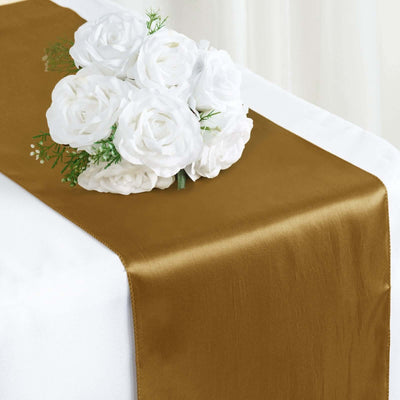 Gold satin table runner with white rose bouquet on a table.