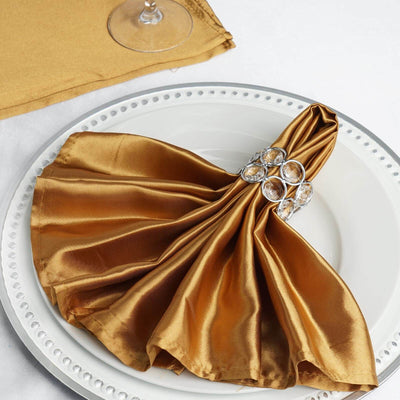 Elegant gold satin napkin with crystal napkin ring on a white plate.
