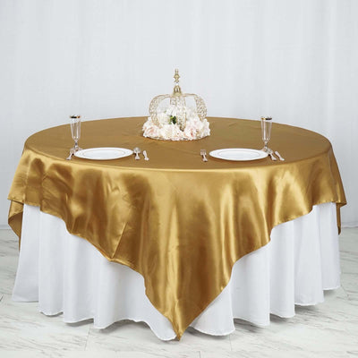 Elegant gold satin tablecloth draped over a round table with decorative centerpiece.