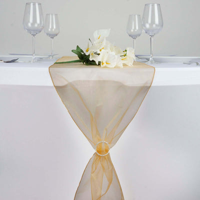 Elegant gold table runner with floral arrangement and wine glasses.