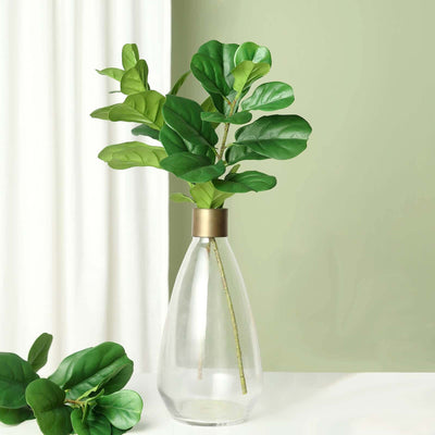 Glass vase with green leaves on a table against a light green background.