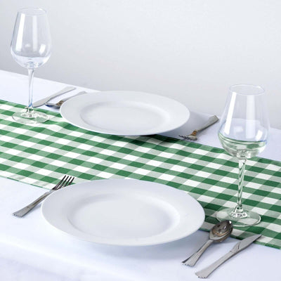 Dining table setting with white plates, green checkered runner, and glassware.