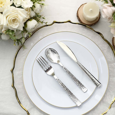 Elegant silver cutlery set on a white plate with floral arrangement and candle.
