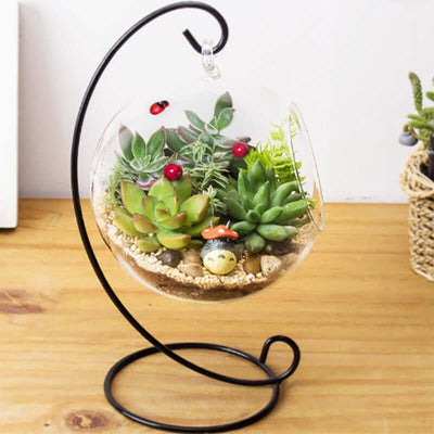 Glass terrarium with succulents and decorative elements on a metal stand.