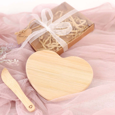Heart-shaped bamboo serving board with a wooden spoon on a soft pink backdrop.