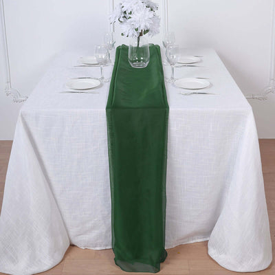 Green table runner on a white table setting with plates and glasses.