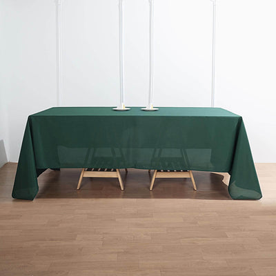 Green tablecloth draped over a wooden table with candlesticks on a plain backdrop.