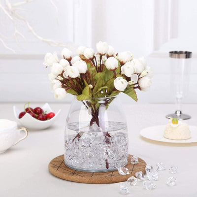 White flower arrangement in a glass vase with decorative stones.