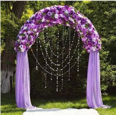 Purple floral wedding arch with draped fabric and hanging crystals.