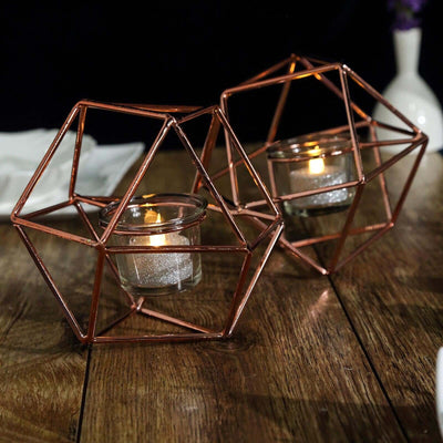Geometric copper candle holders with glass votives on a wooden surface.