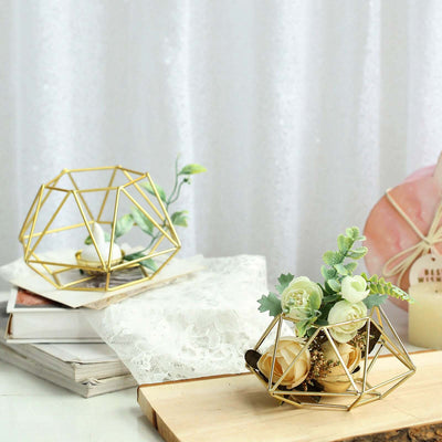 Geometric gold plant holder with faux flowers and greenery on a wooden surface.