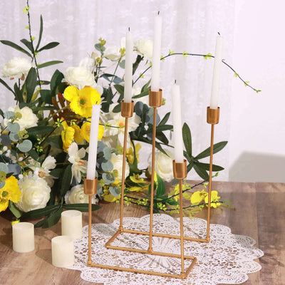 Gold candle holder with white candles surrounded by floral decor.