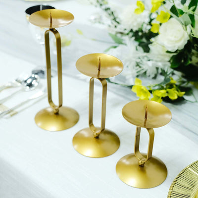 Gold candle holders in varying heights on a table with floral arrangement.