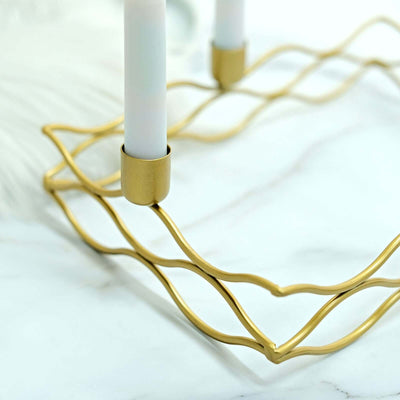 Gold wave-pattern candle holder with white candles on a marble surface.