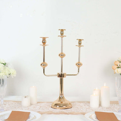 Gold three-arm candelabra centerpiece with candles on a table.