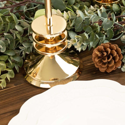 Gold candle holder with pine cone and greenery on a wooden table.