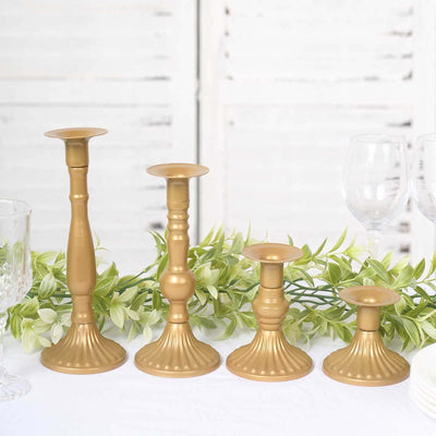 Set of four elegant gold candle holders on a table with greenery.