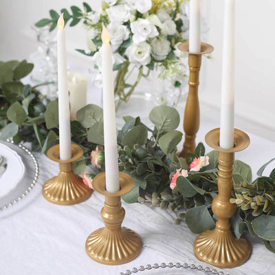 Gold candlesticks with white candles and greenery on a table.