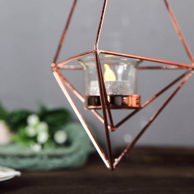 Geometric rose gold candle holder with glass detail and a flickering candle flame.