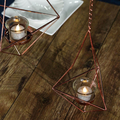 Hanging geometric candle holders with tealights on a wooden surface.