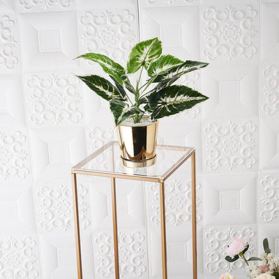Gold potted plant on a transparent stand against textured white background.