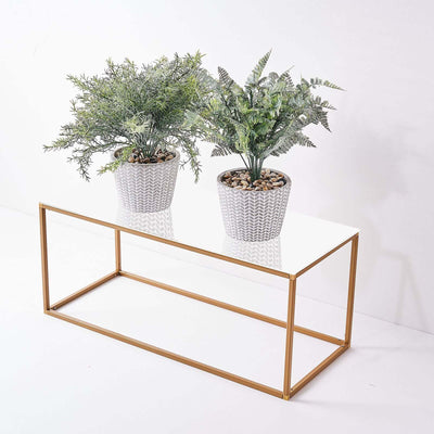 Modern gold coffee table with two potted plants on a white surface.