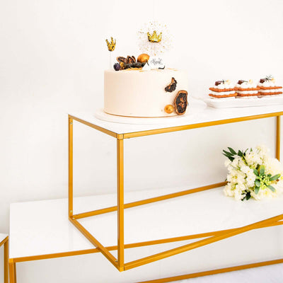 Elegant cake on gold and white display stand with decorative treats and flowers.