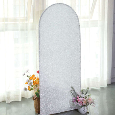 Glittery arch-shaped mirror against a window with flowers in pots.
