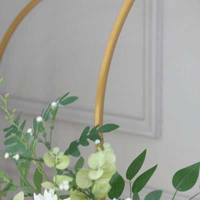 Decorative gold arch with greenery and flowers in a minimalist setting.