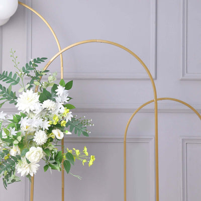 Gold floral display stand with white and green flowers against a grey wall.